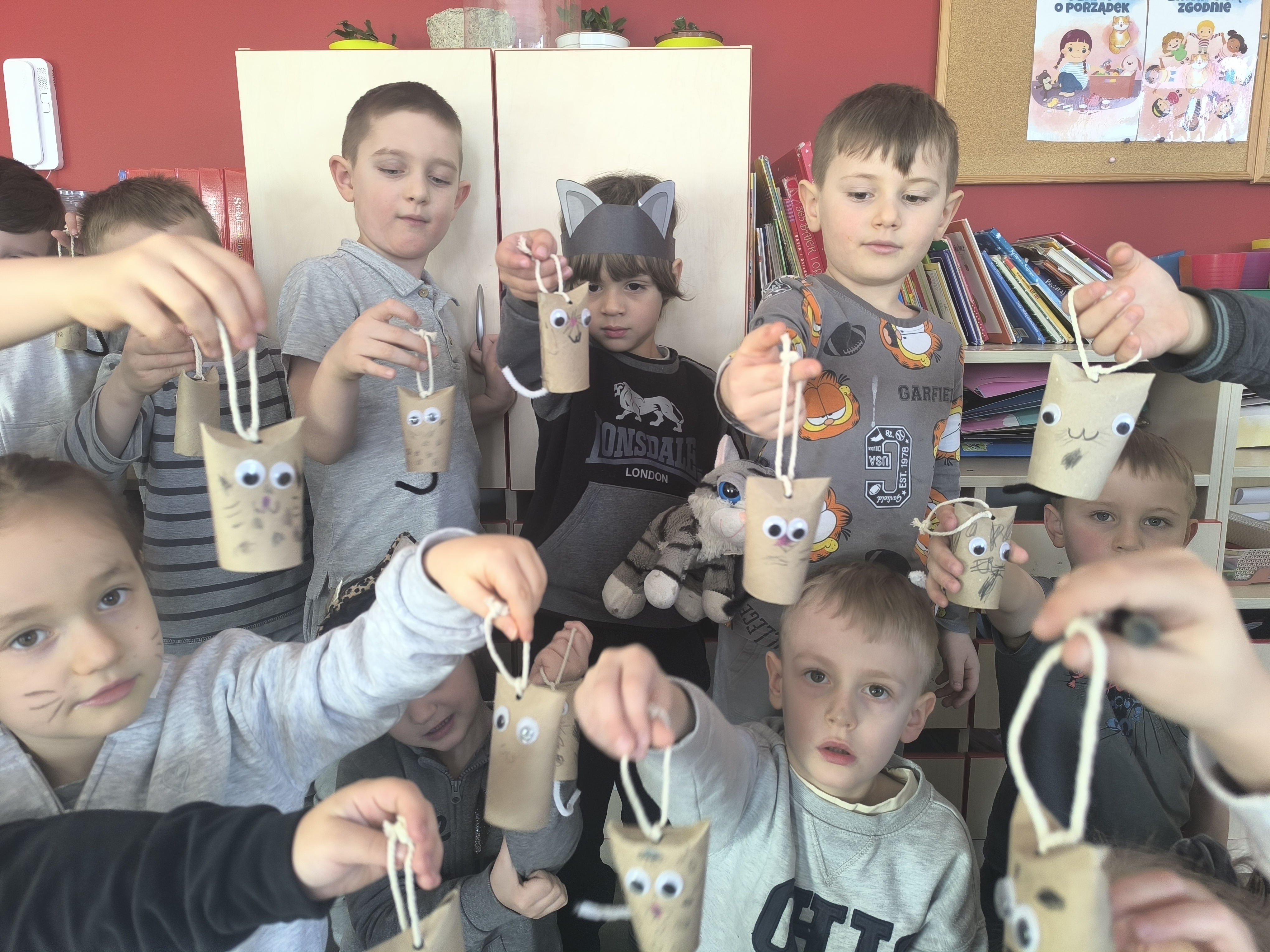 Dzień Kota - Przedszkolaki z zawieszkami kotkami wykonanymi z rolek po papierze, dumnie je prezentują.