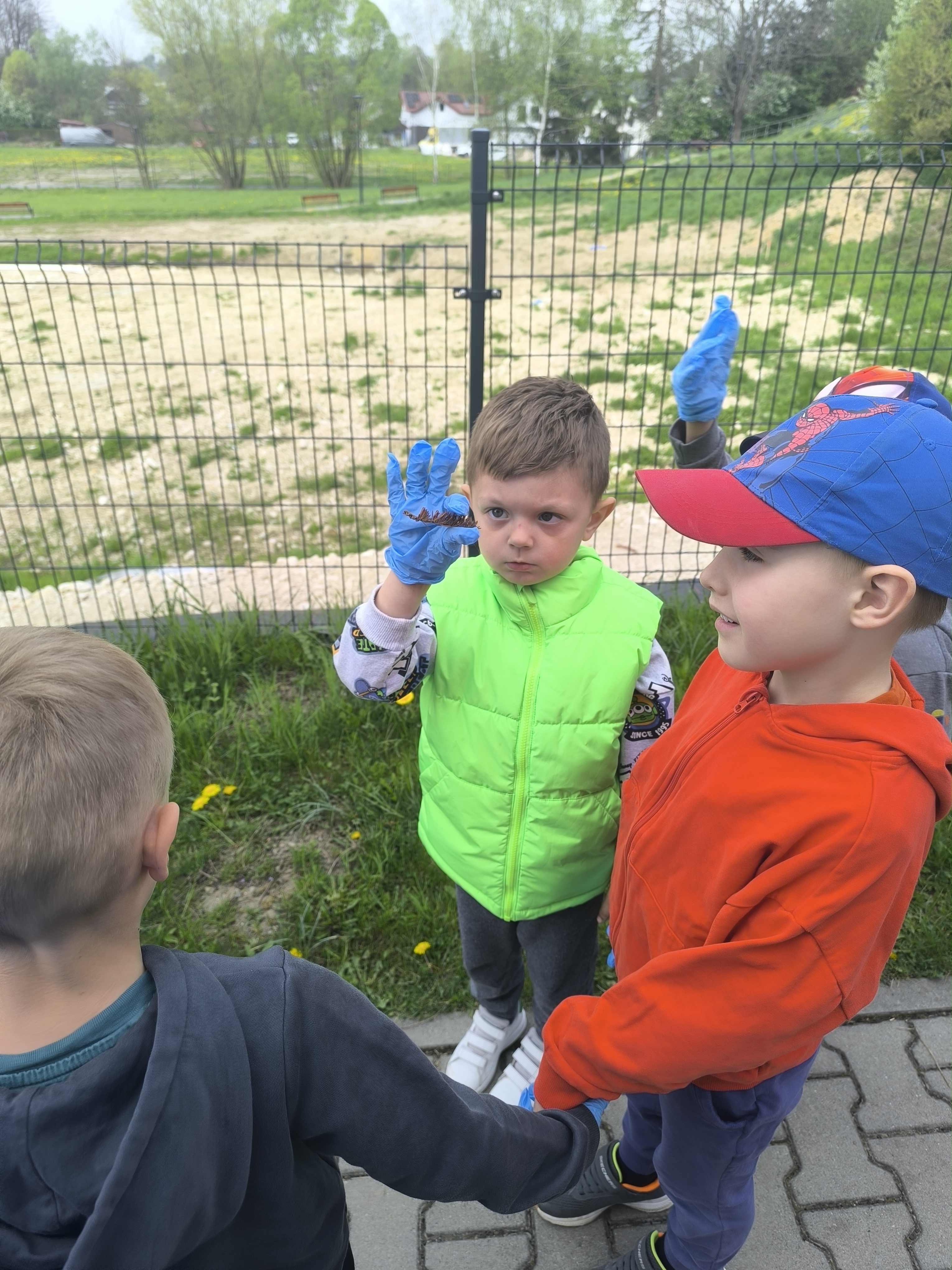 Sprzątanie Świata - Dzieci z przedszkola pokazujące znalezione śmieci podczas akcji sprzątania na terenie zielonym.