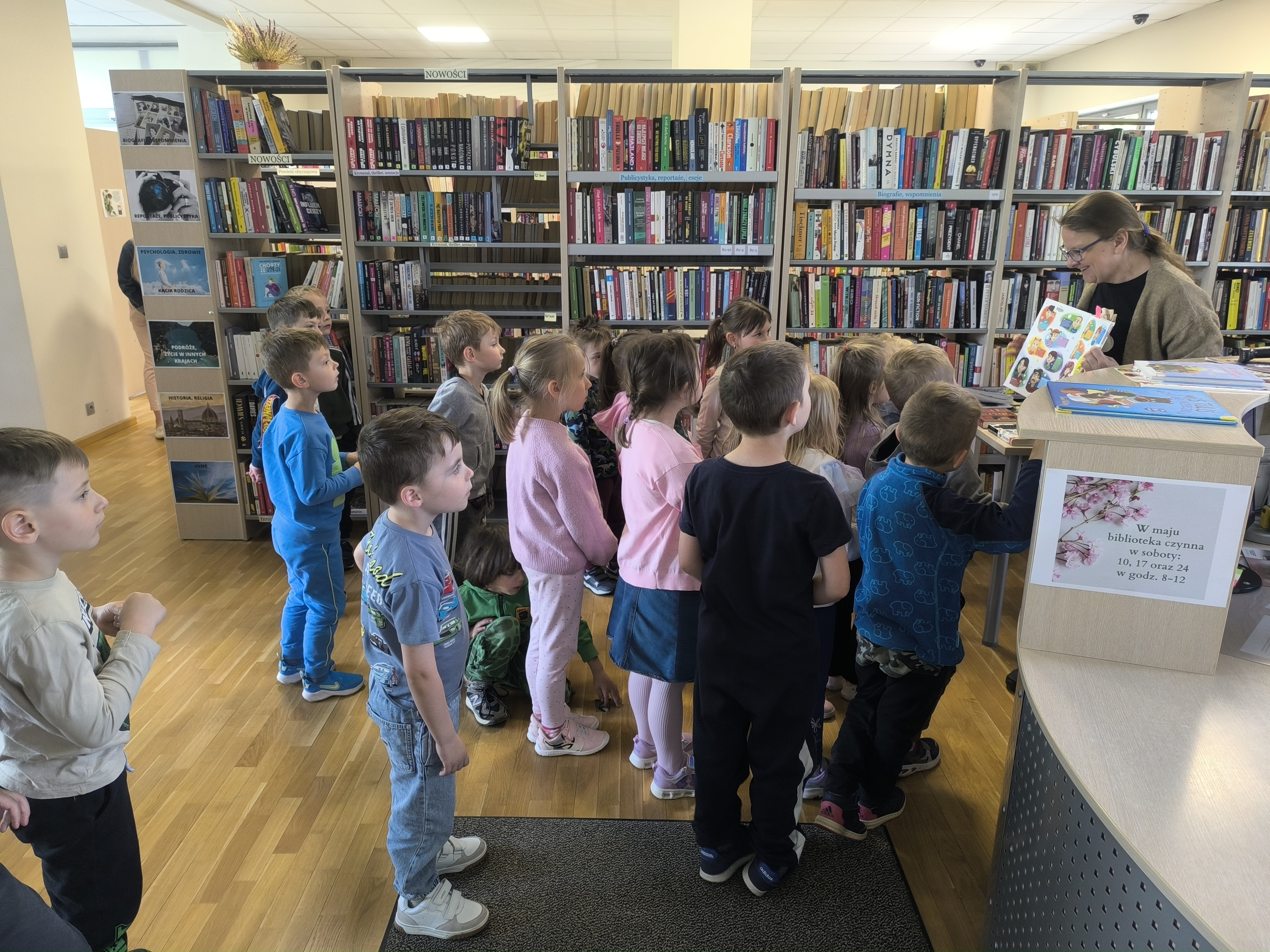 Dzień Biblioteki - Dzieci z przedszkola uważnie słuchające opowieści oraz oglądające kolorowe książki podczas wizyty w bibliotece.