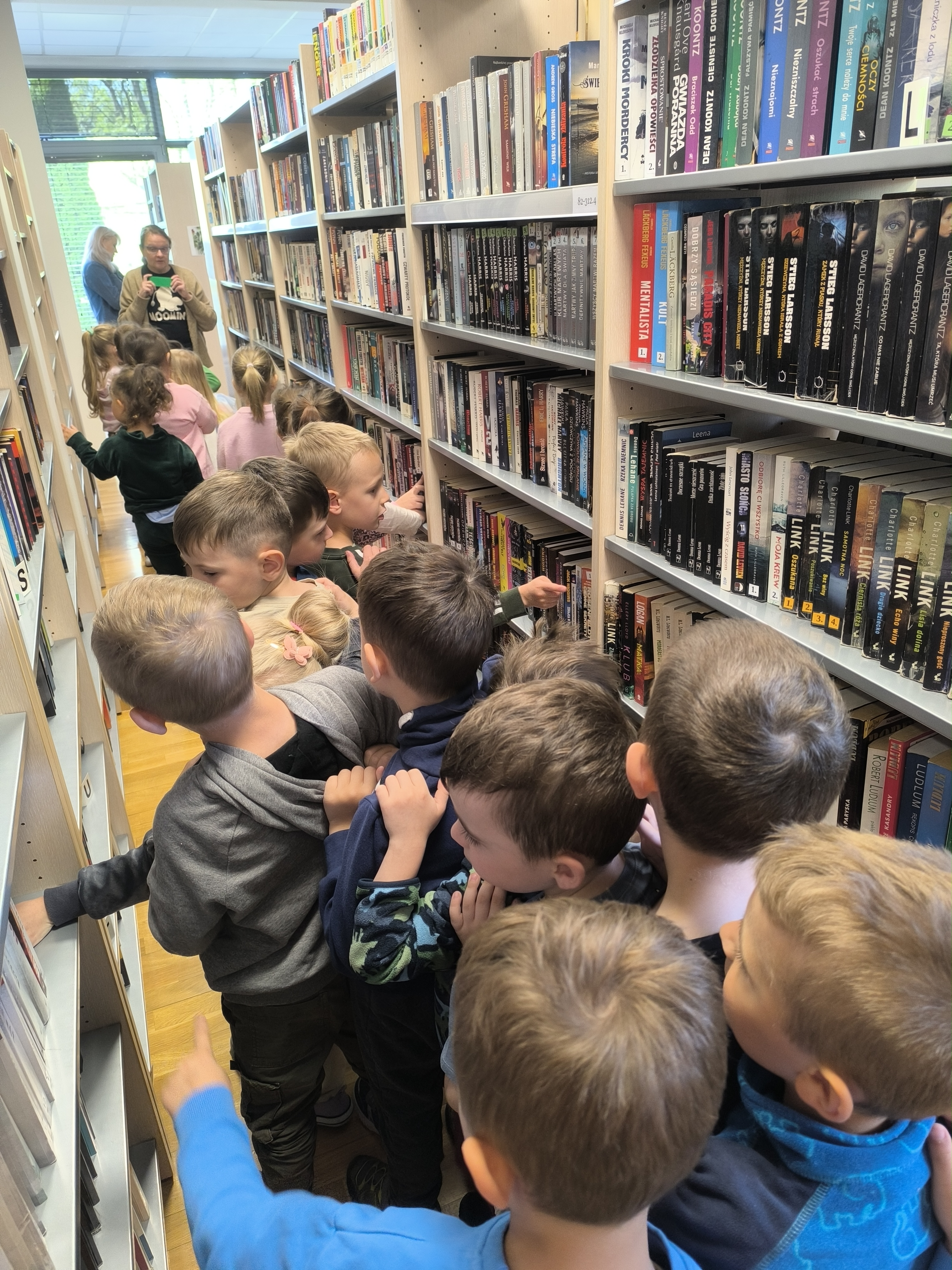 Dzień Biblioteki - Dzieci z przedszkola bawiące się w pociąg, przechodząc między regałami z książkami w bibliotece.