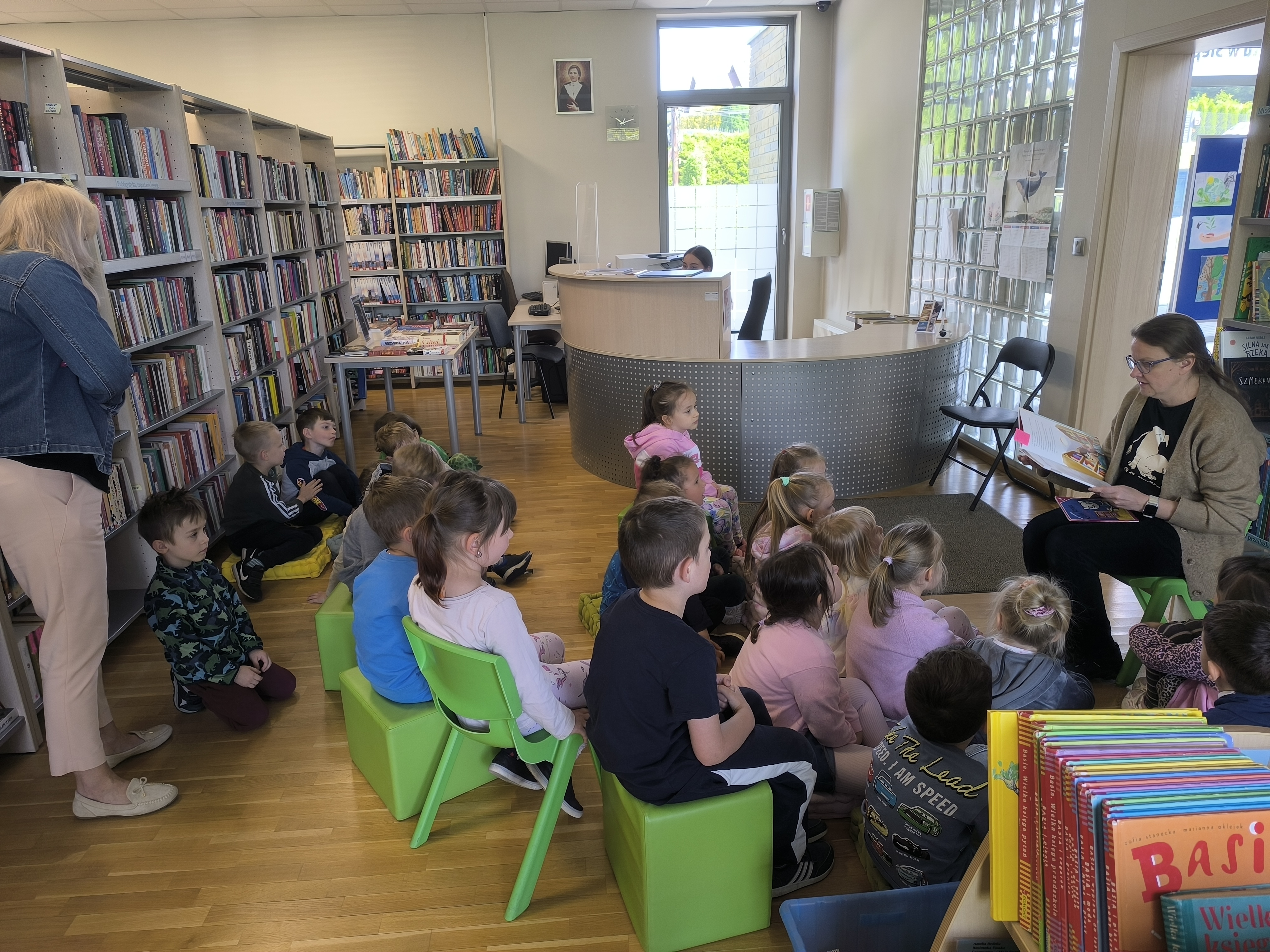Dzień Biblioteki - Dzieci z przedszkola siedzące na kolorowych krzesełkach i poduszkach, słuchające bajek czytanych przez bibliotekarkę.