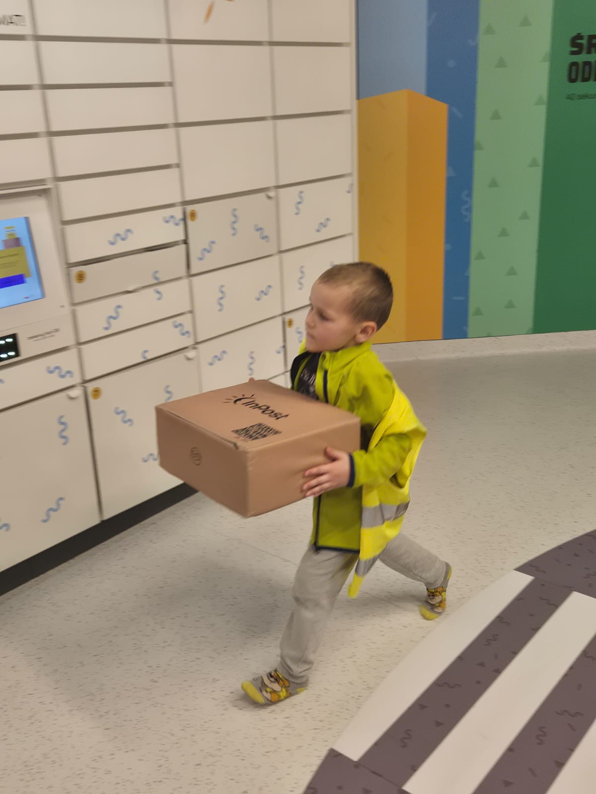 Chłopiec idzie z paczką do paczkomatu.